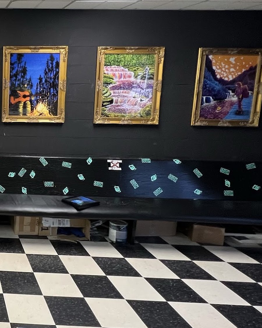 Interior of the south shop: gilded picture frames on a black wall above a bench, over a black and white checkerboard floor