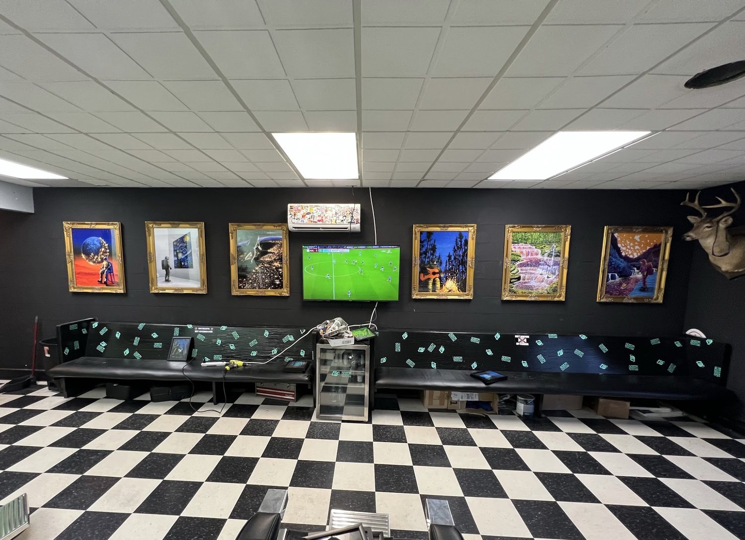 The waiting area of the south shop: framed paintings on a black wall, a long bench and a checkerboard tile floor